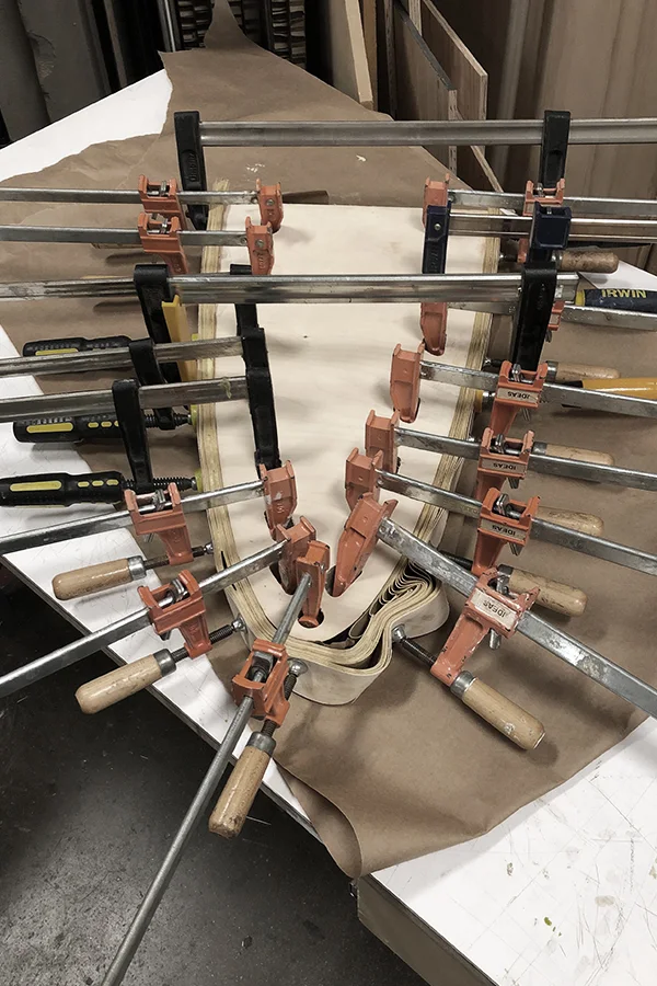 A laminated bow held in a row of clamps while the glue sets