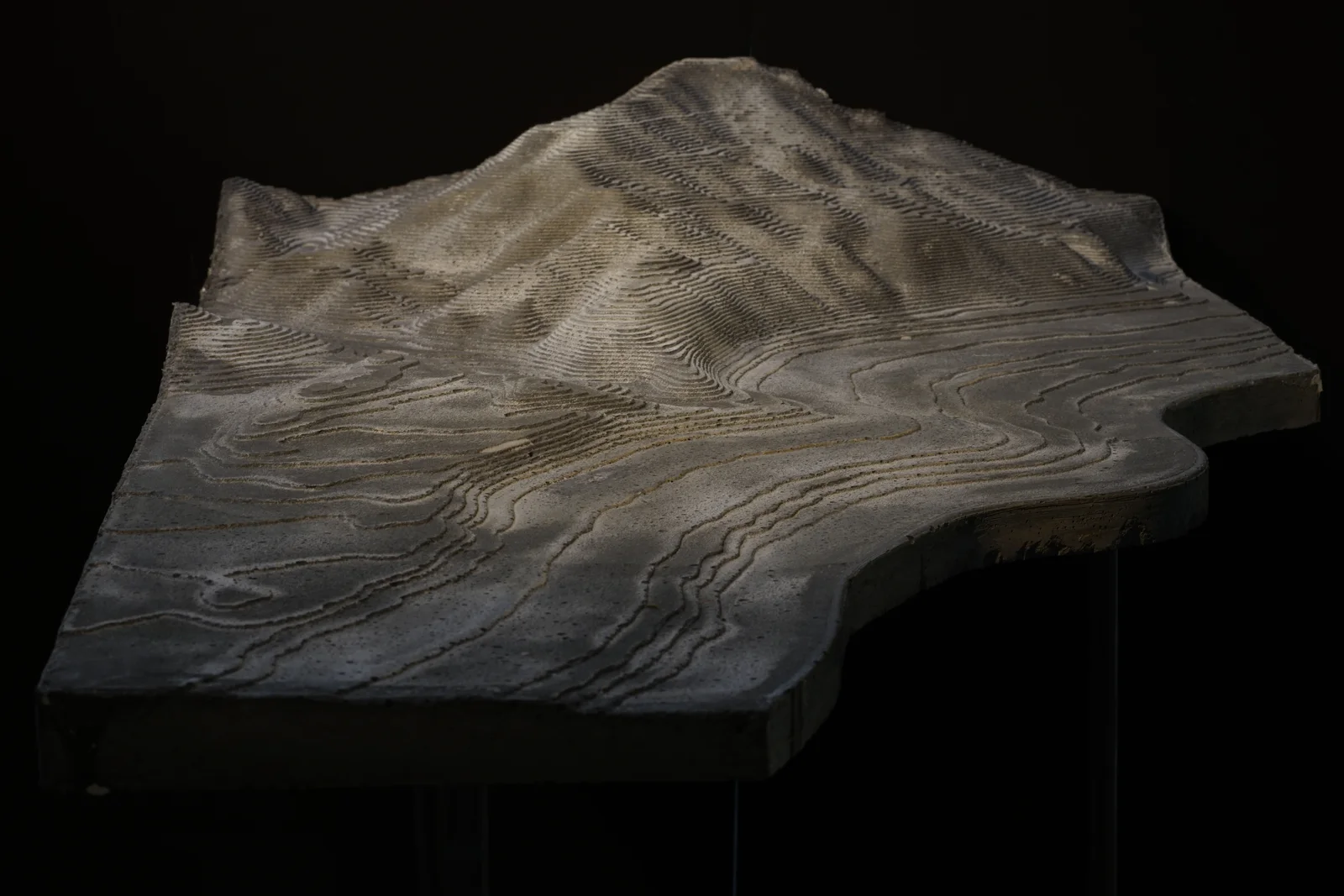 A CNC-milled relief of a coastline in pale wood, lit from the side on a dark ground