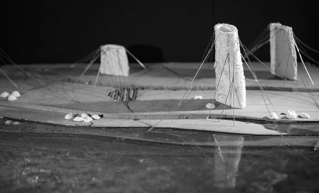 A dark model of a shoreline with three masts and cables rising from it