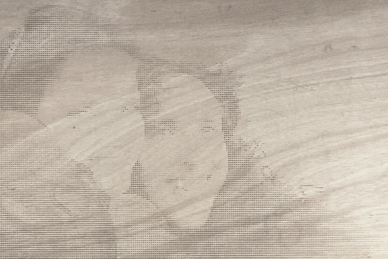 A wide plywood panel with a close portrait drilled faintly into the grain