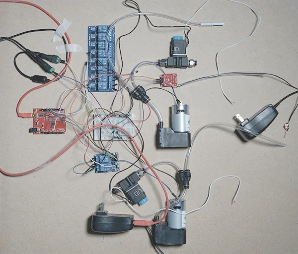 An Arduino board wired to relays, pumps and valves on a cardboard sheet