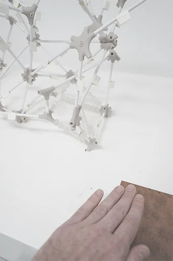 A hand resting on a copper plate beside the wire-and-node model
