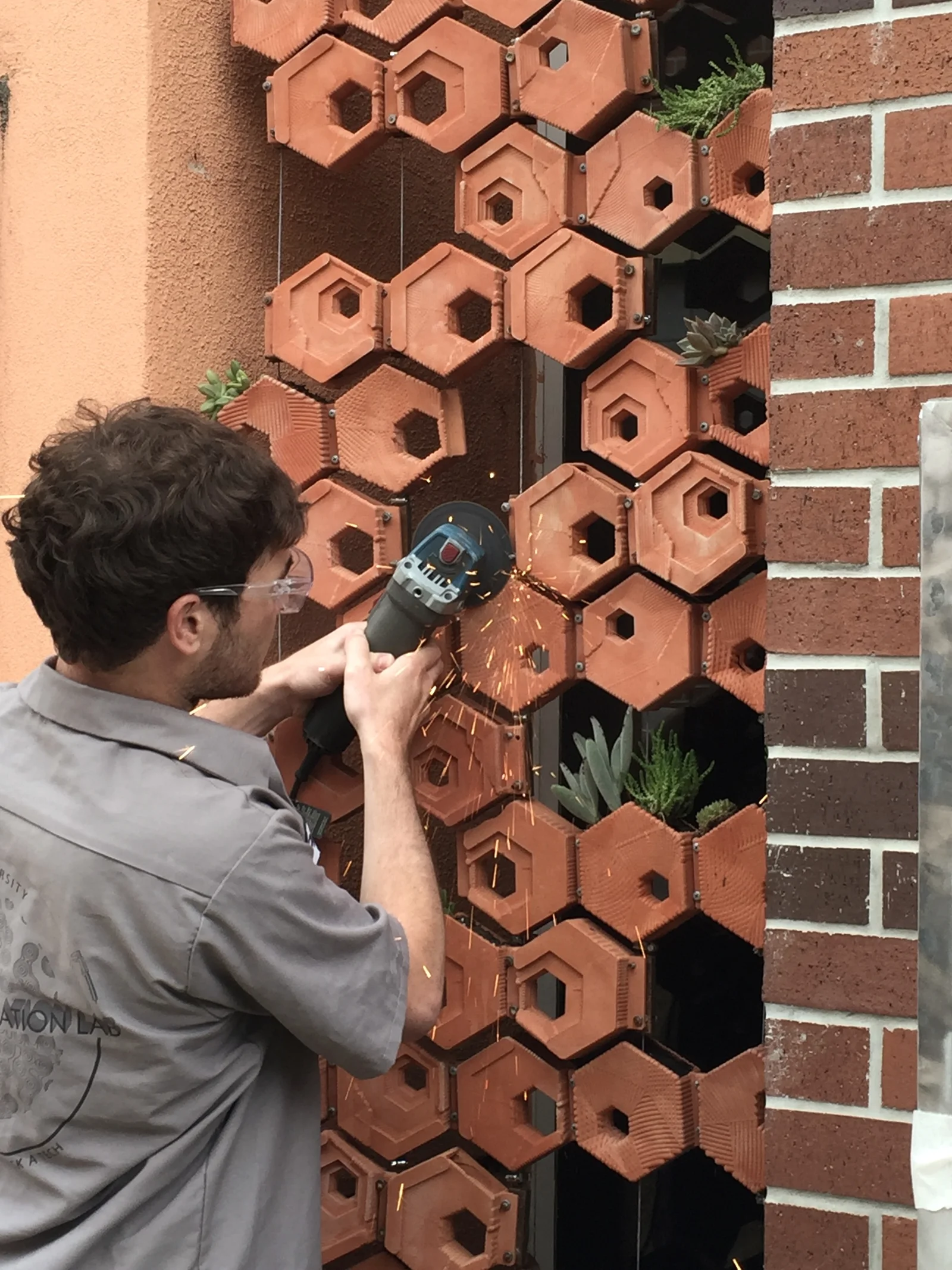 Michael drilling an anchor into the brick wall beside the hanging modules