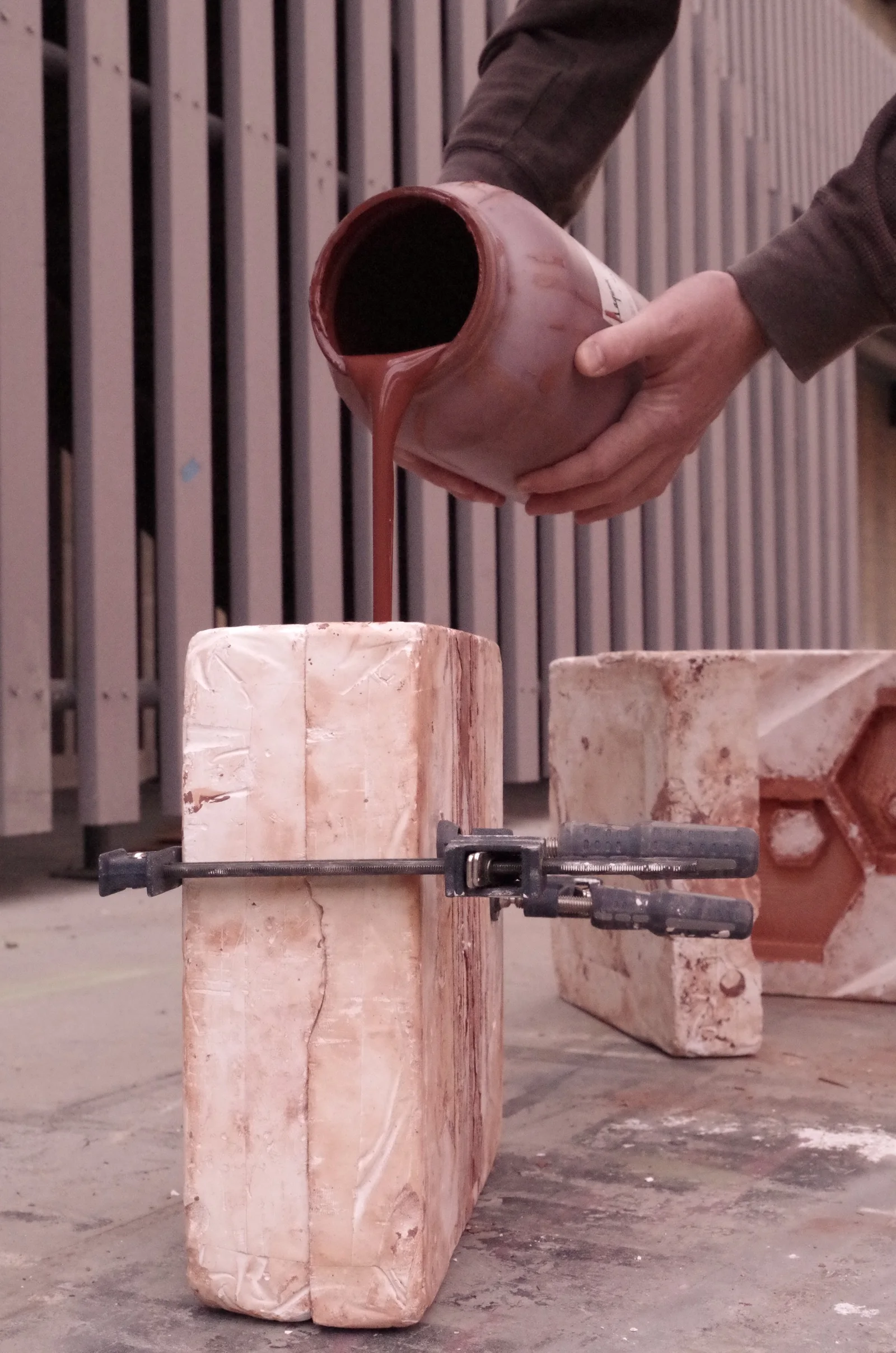 Hands pouring terracotta slip from a jug into a plaster mold